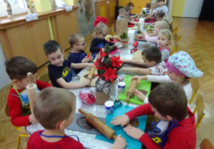 Dzieci przy ozdobionym świątecznie stole rozwałkowują ciasto na pierniki.